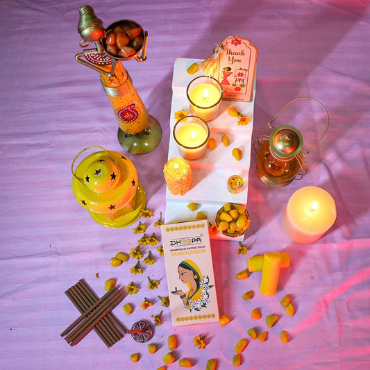Decorative setup with candles, a box, and small figurines on a pink surface
